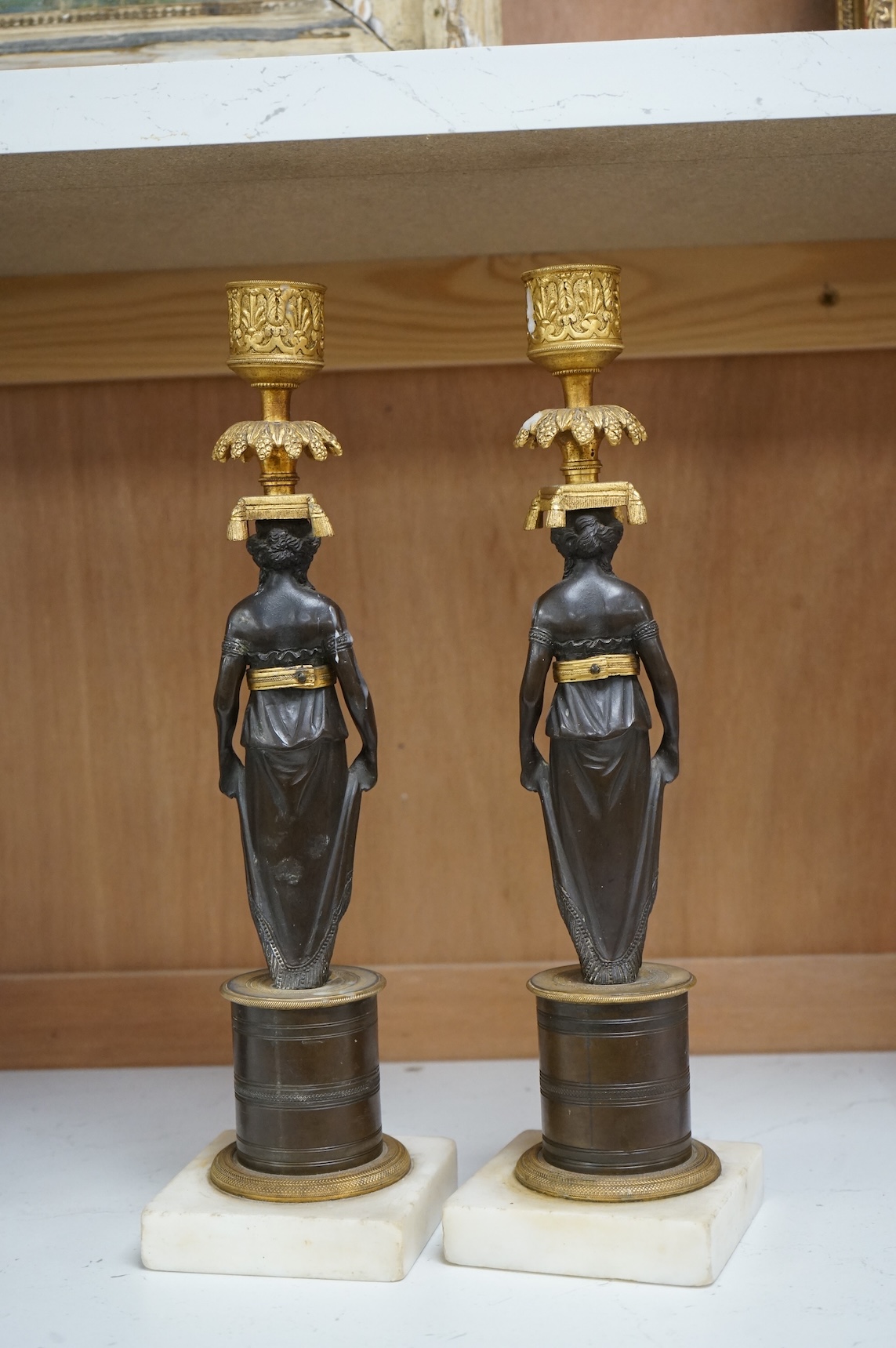 A pair of Regency bronze and gilt candlesticks in the form of standing classical figures mounted on marble bases, 31.5cm high.